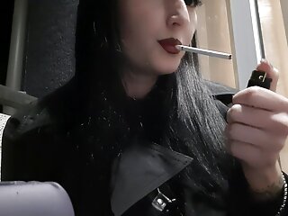 Dominatrix Nika Smokes A Cigarette On The Balcony. Mistress Sexy Red Lips Blow Smoke In Your Face